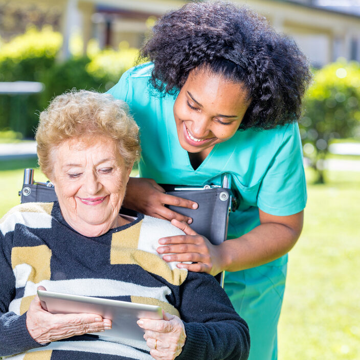 Nurse explaining tablet use to elder woman on wheelchair.