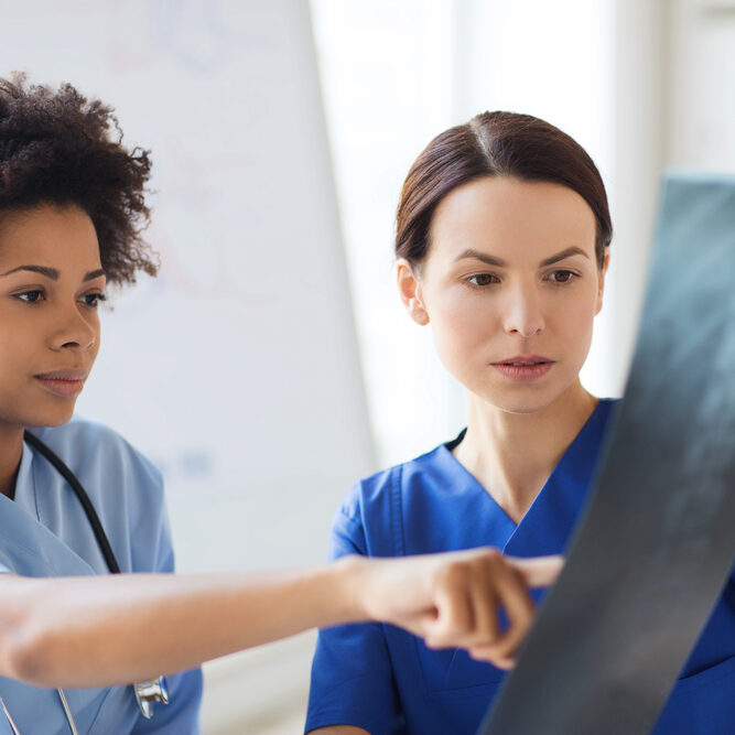 radiology, surgery, people and medicine concept - female doctors looking to and discussing x-ray image at hospital